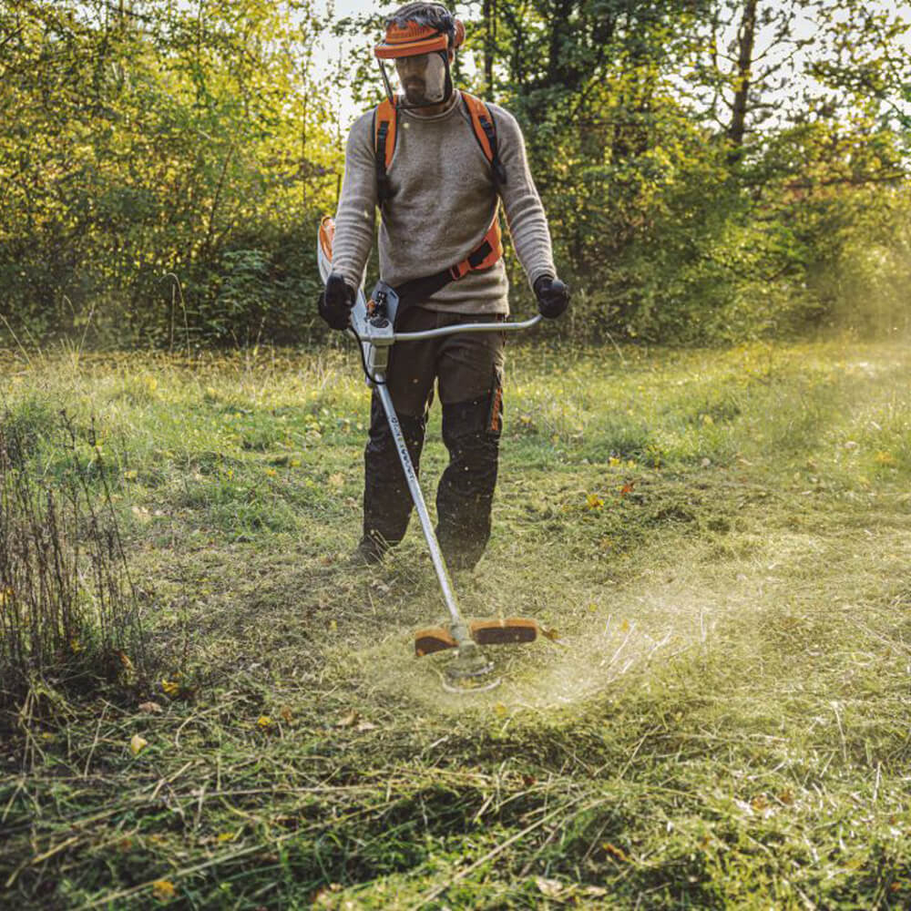 Eine Person mäht mit der akkubetriebenen Stihl Motorsense FSA 200 (AP-System, Solo) eine grüne Wiese.