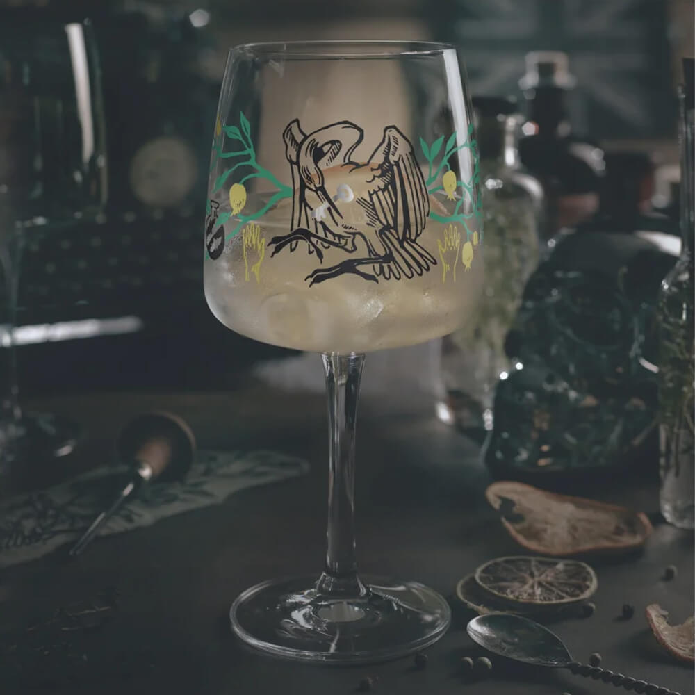 Ein gefülltes Ritzenhoff Ginglas "Fabelkraft" von Karin Rytter steht auf einer stimmungsvollen, dunklen Bar. Das surreale Dekor mit seinen magischen Wesen und Symbolen kommt in dieser Atmosphäre besonders zur Geltung und lädt zum Entdecken bei einem Drink