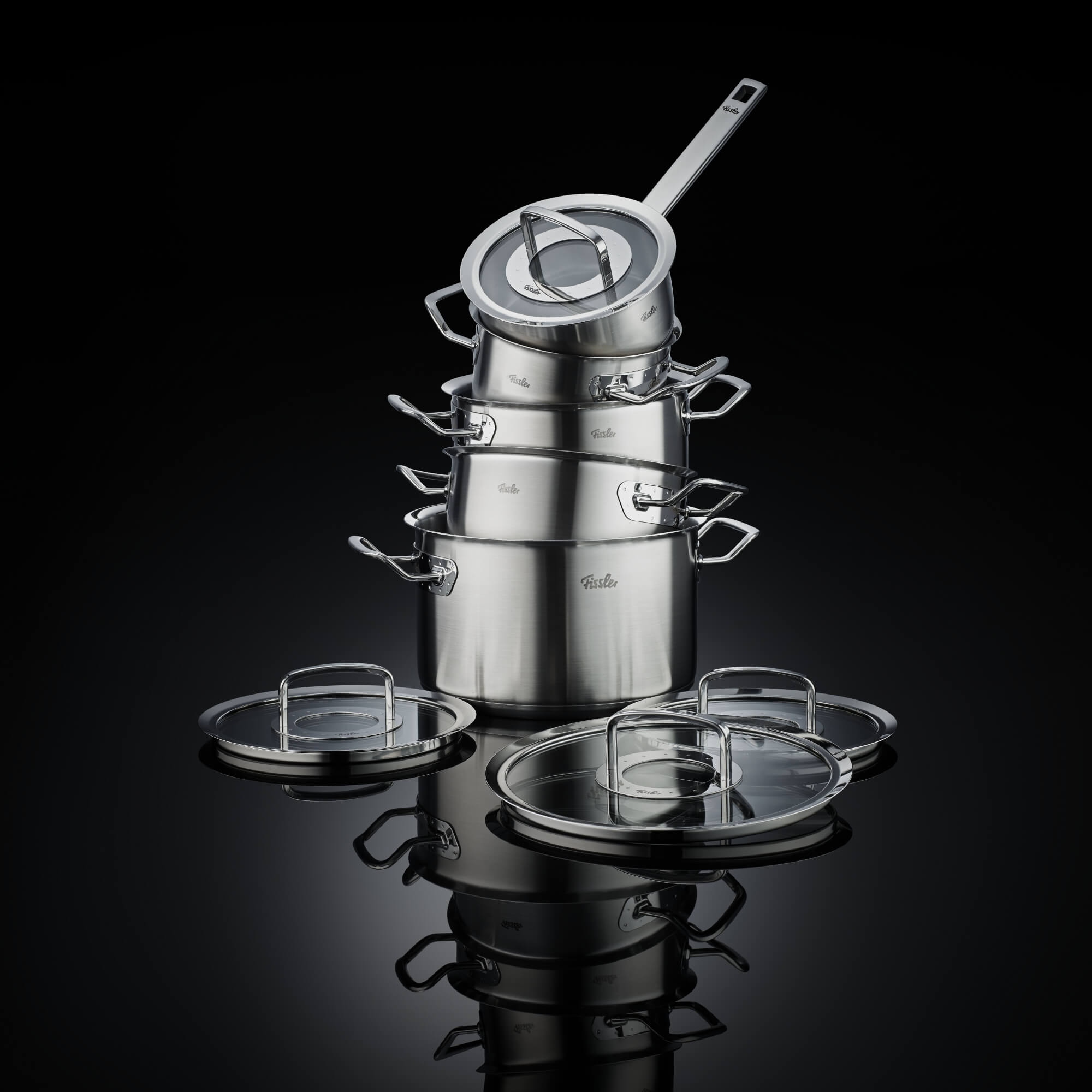 Fissler Profi Collection – Das komplette Set in edlem Design Die komplette Fissler Profi Collection in stilvoller Inszenierung vor schwarzem Hintergrund, alle Teile der Kollektion in edlem Design.