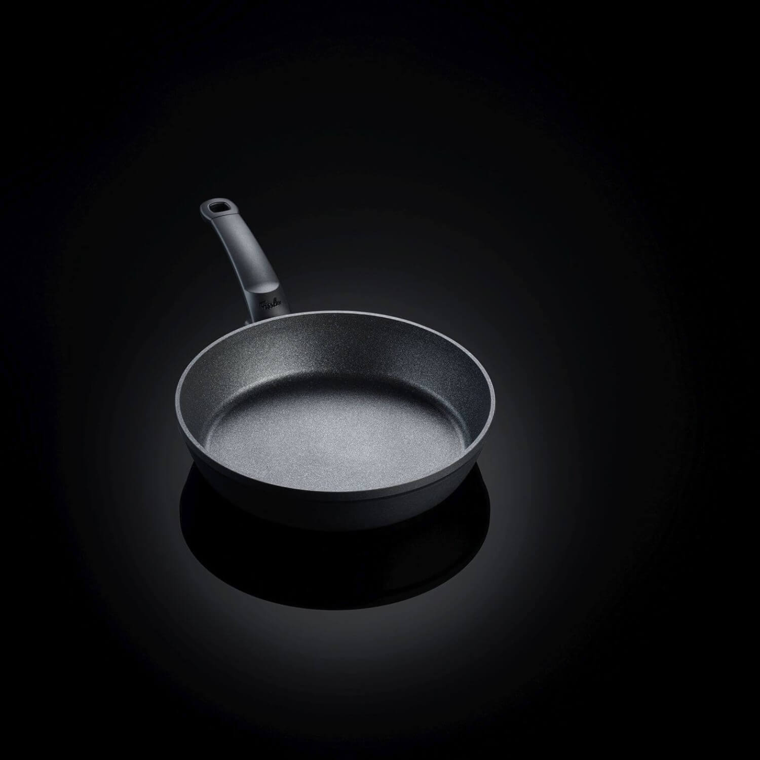 Eine stilvoll beleuchtete, schwarze Fissler Pfanne vor dunklem Hintergrund – modernes Design trifft auf hochwertige Verarbeitung