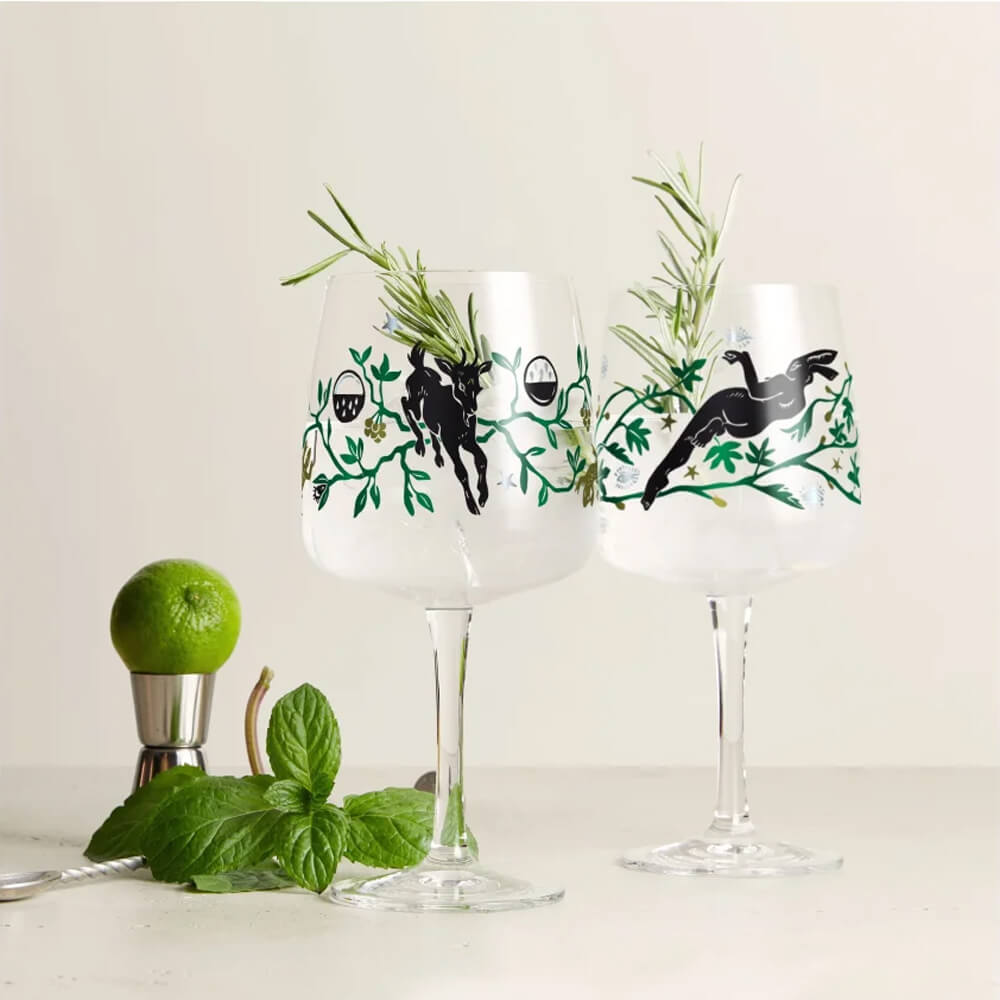 Ein gefülltes Ritzenhoff Ginglas "Fabelkraft" von Karin Rytter steht vor einem hellen, neutralen Hintergrund. Auf der linken Bildseite sind Barzubehör und eine Limette zu sehen, die das Ambiente ergänzen. Das Glas zeigt den Faun im Ziegenpelz und lädt daz